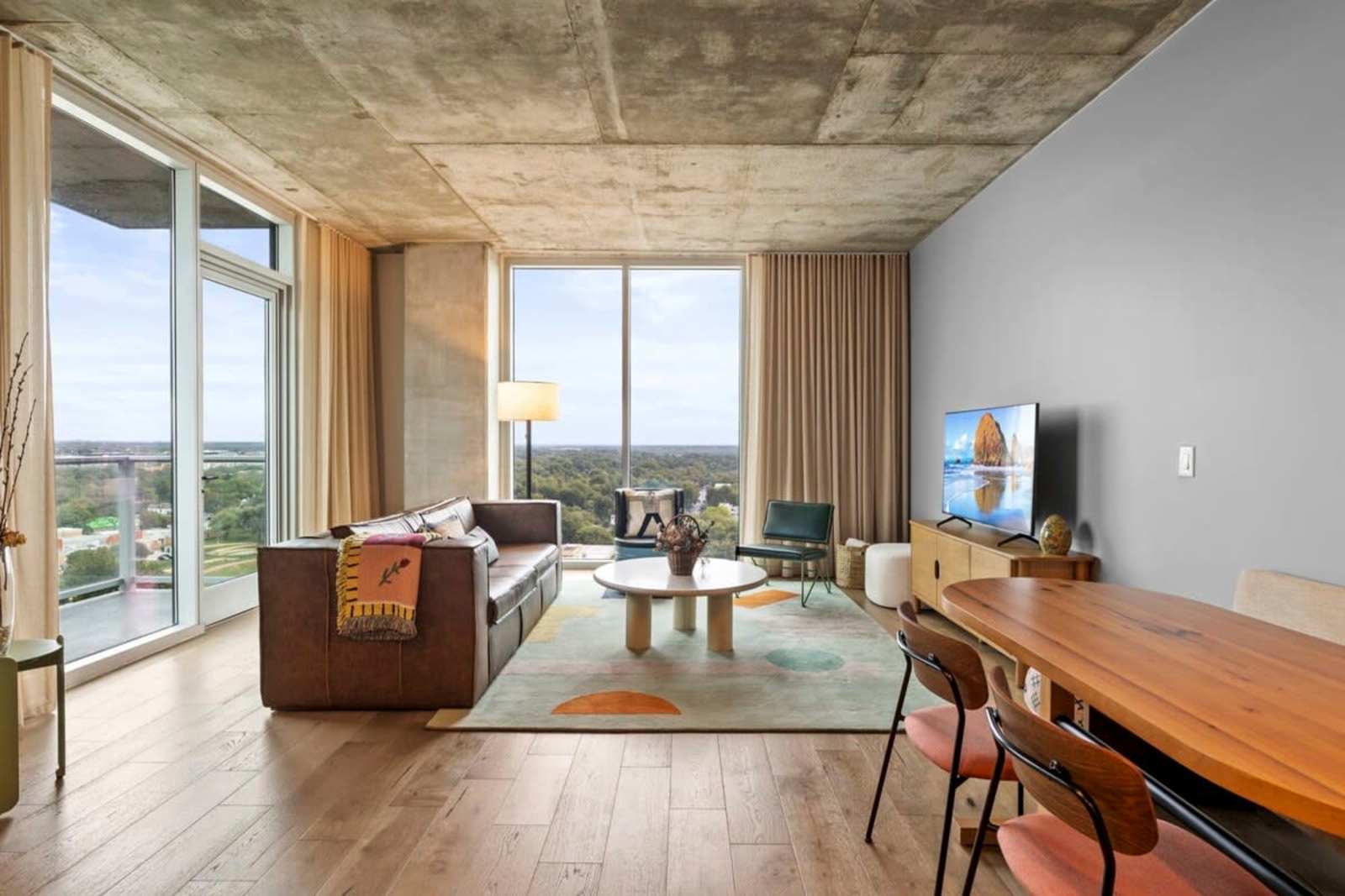 Living and dining area of unit 1804 at Natiivo Austin with a leather sofa, long oak table and morning light through the glass