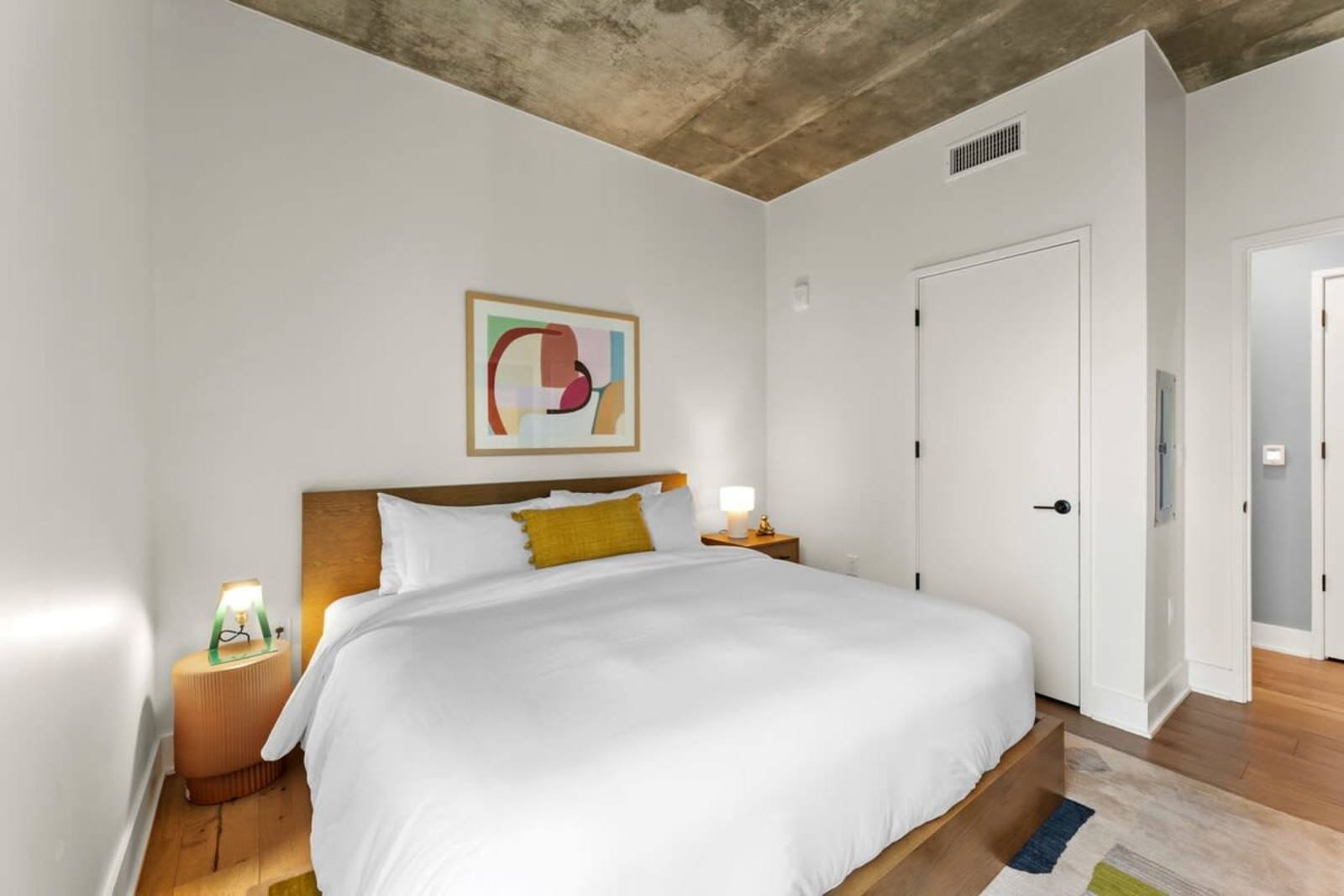 King bedroom in unit 1804 with white linens, framed artwork and a doorway to the hall