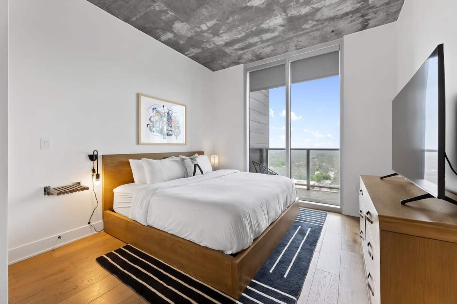 King bedroom in unit 2006 with floor-to-ceiling glass, striped rug and skyline views from the 20th floor