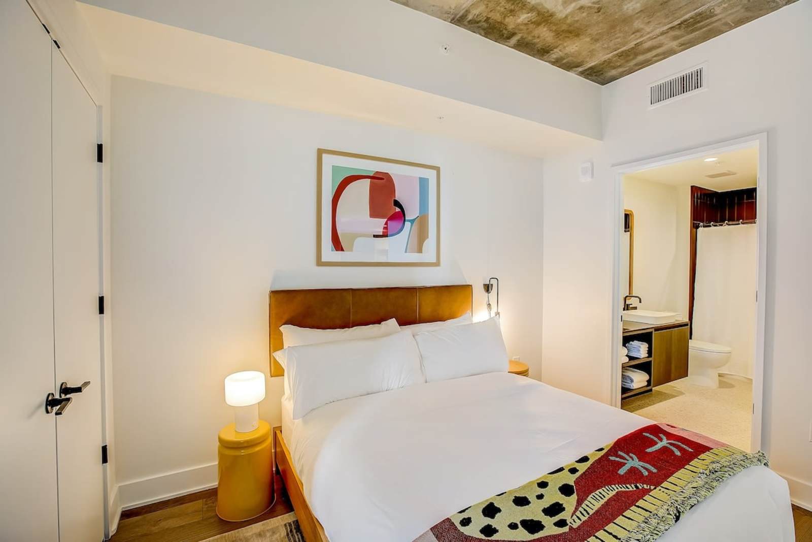 First bedroom in unit 1406 with a queen bed, framed artwork and an ensuite bathroom visible through the doorway