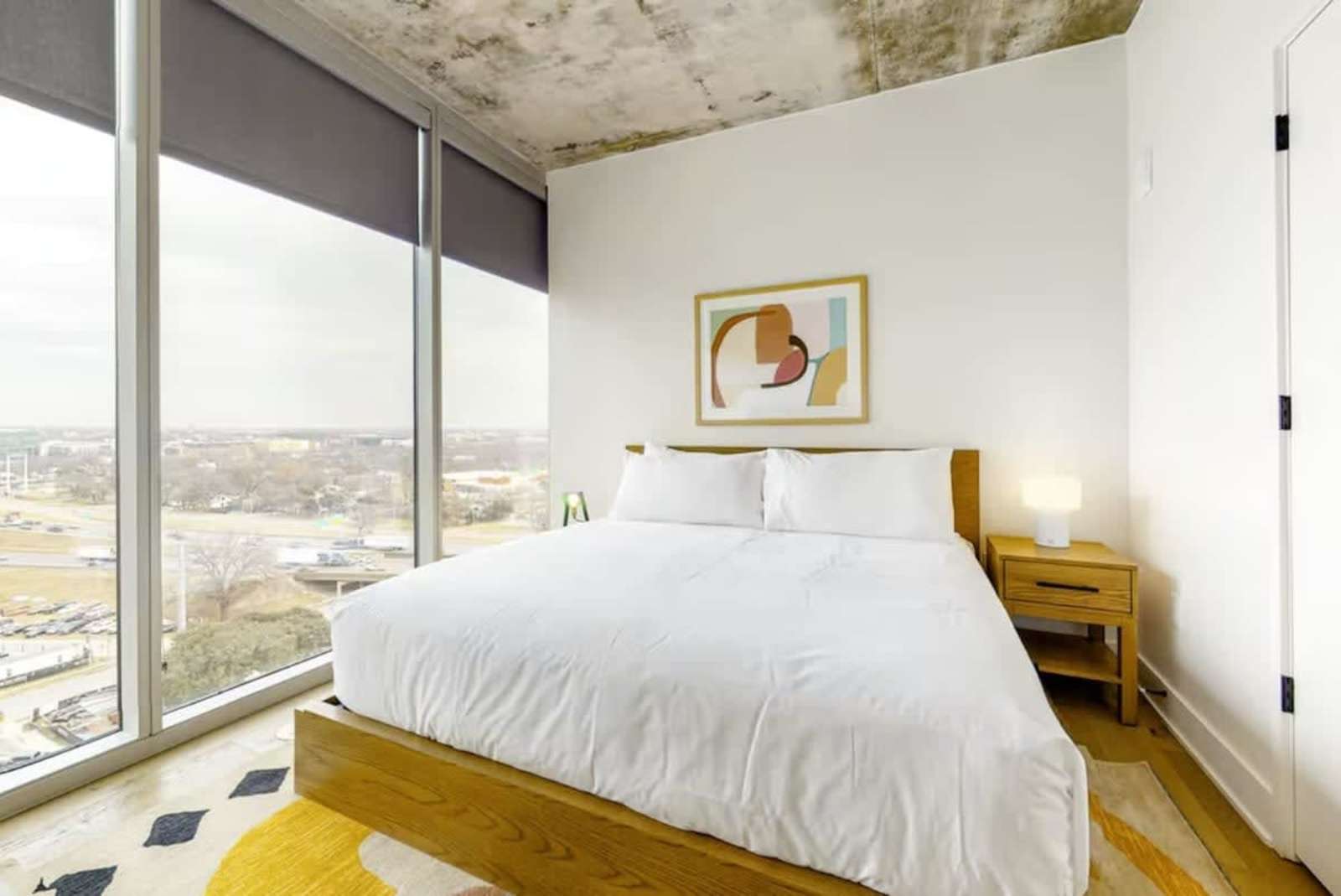 King bedroom in unit 1205 with a corner of floor-to-ceiling glass and long views across Austin