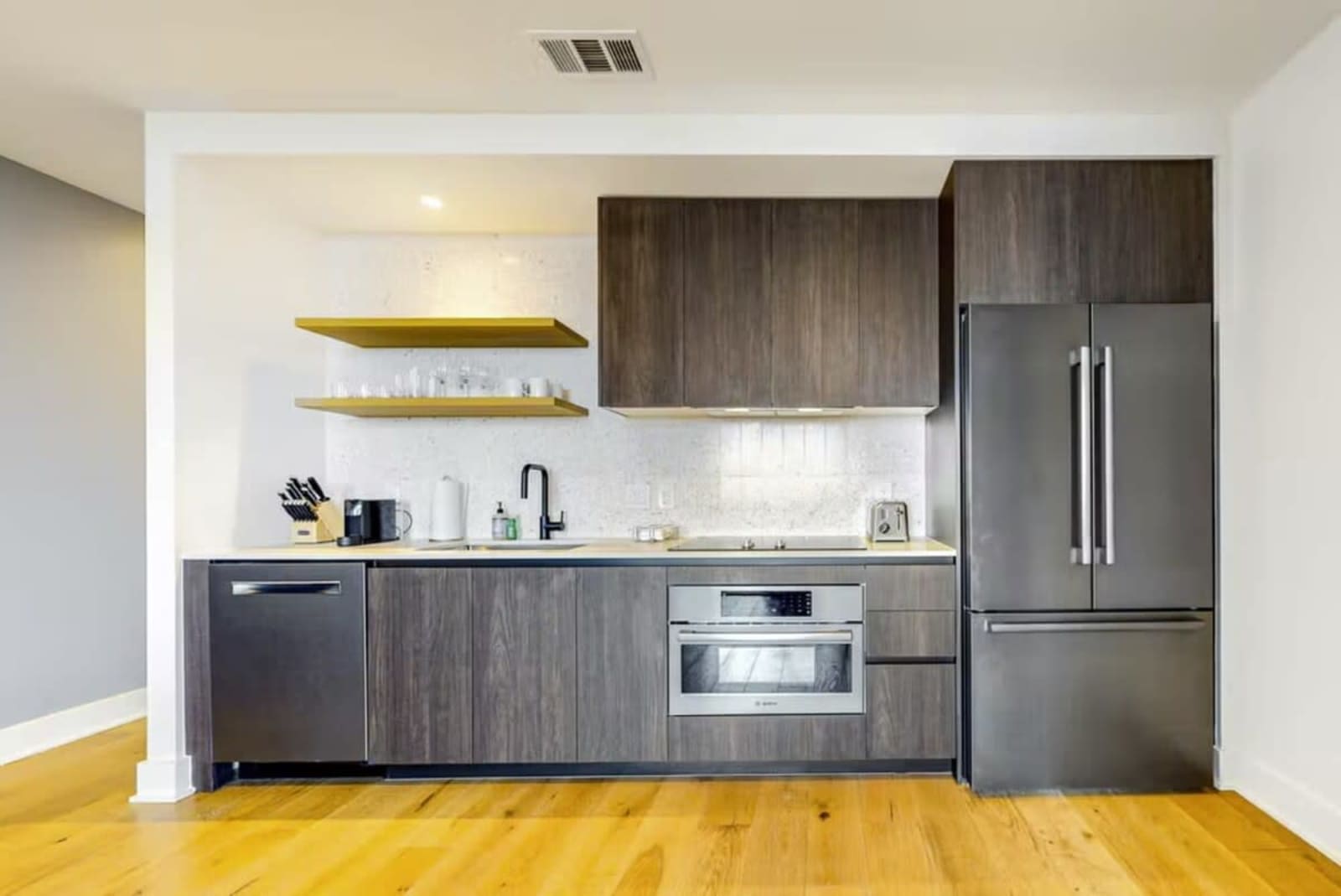 Kitchen in unit 1205 with dark cabinetry, wall oven, dishwasher and a full-height stainless refrigerator