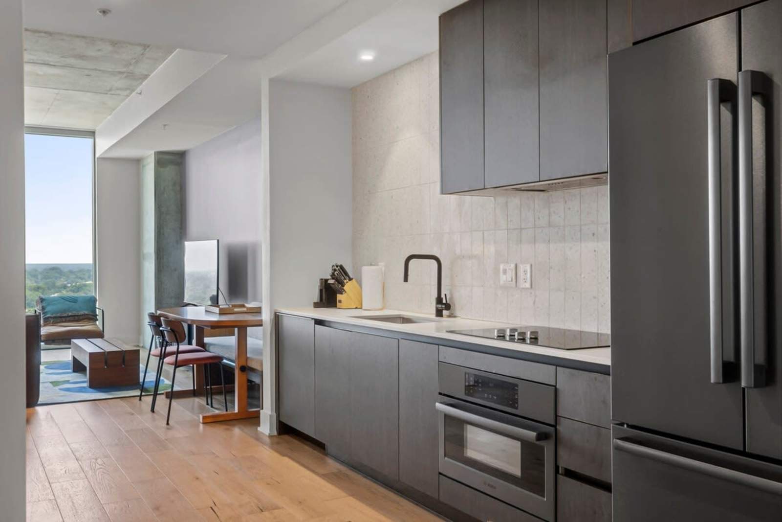 Kitchen in unit 1409 with dark cabinetry, induction cooktop, wall oven and refrigerator, on oak floors