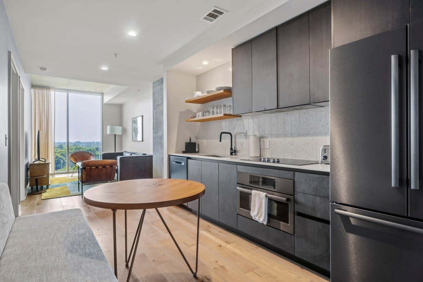 Open kitchen in unit 1105 with dark cabinetry, a full-size refrigerator, oven and round dining table on oak floors