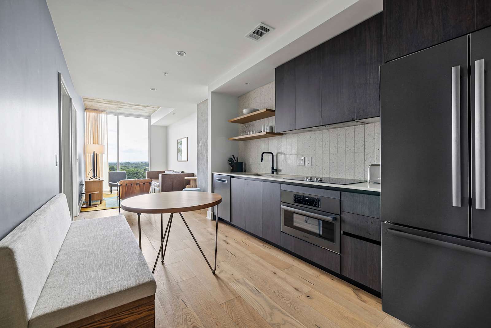 Kitchen in unit 1204 with dark cabinetry, wall oven, full-size refrigerator and a window seat by the glass