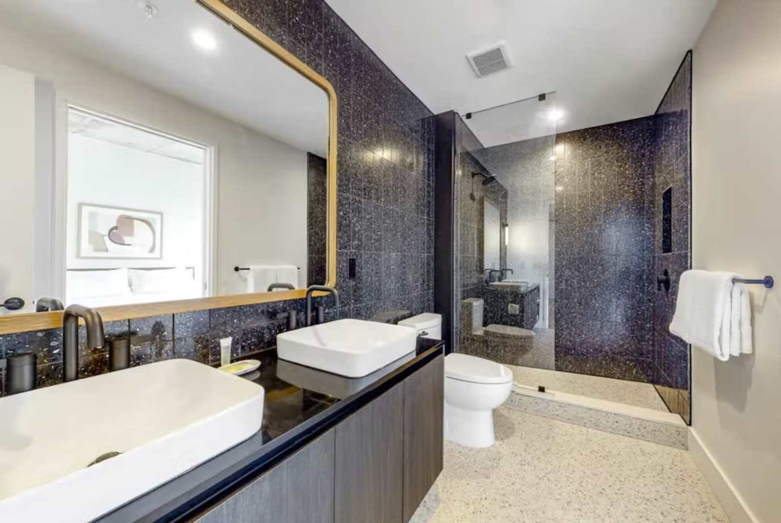 Bathroom in unit 1205 with twin vanity, brass-framed mirror and a glass walk-in shower