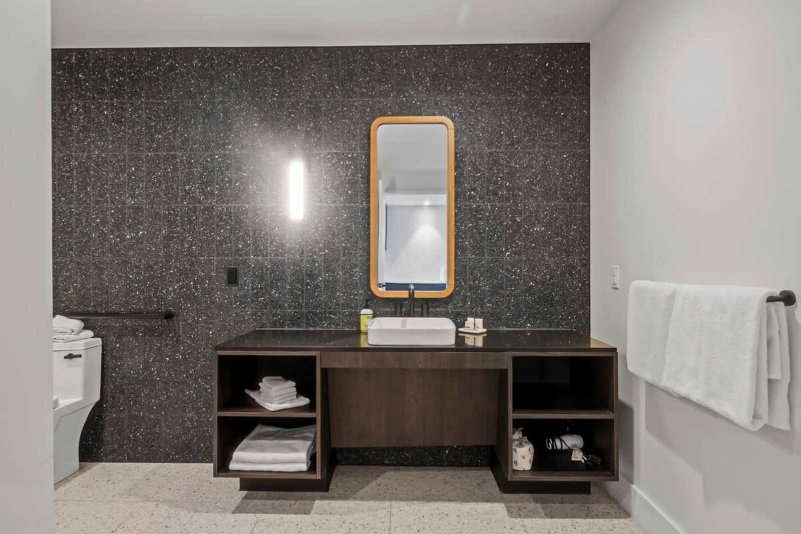 Bathroom in unit 1409 with a vessel sink, dark speckled stone wall, brass-framed mirror and grab rail