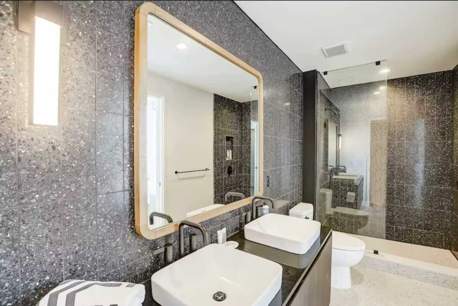 Bathroom in unit 1504 with a vessel sink, brass-framed mirror, walk-in shower and speckled stone wall