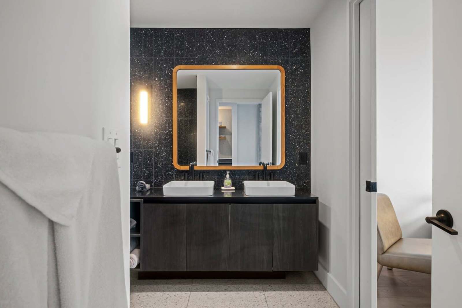 Bathroom vanity in unit 1105 with a vessel sink, brass-framed mirror and dark textured tile