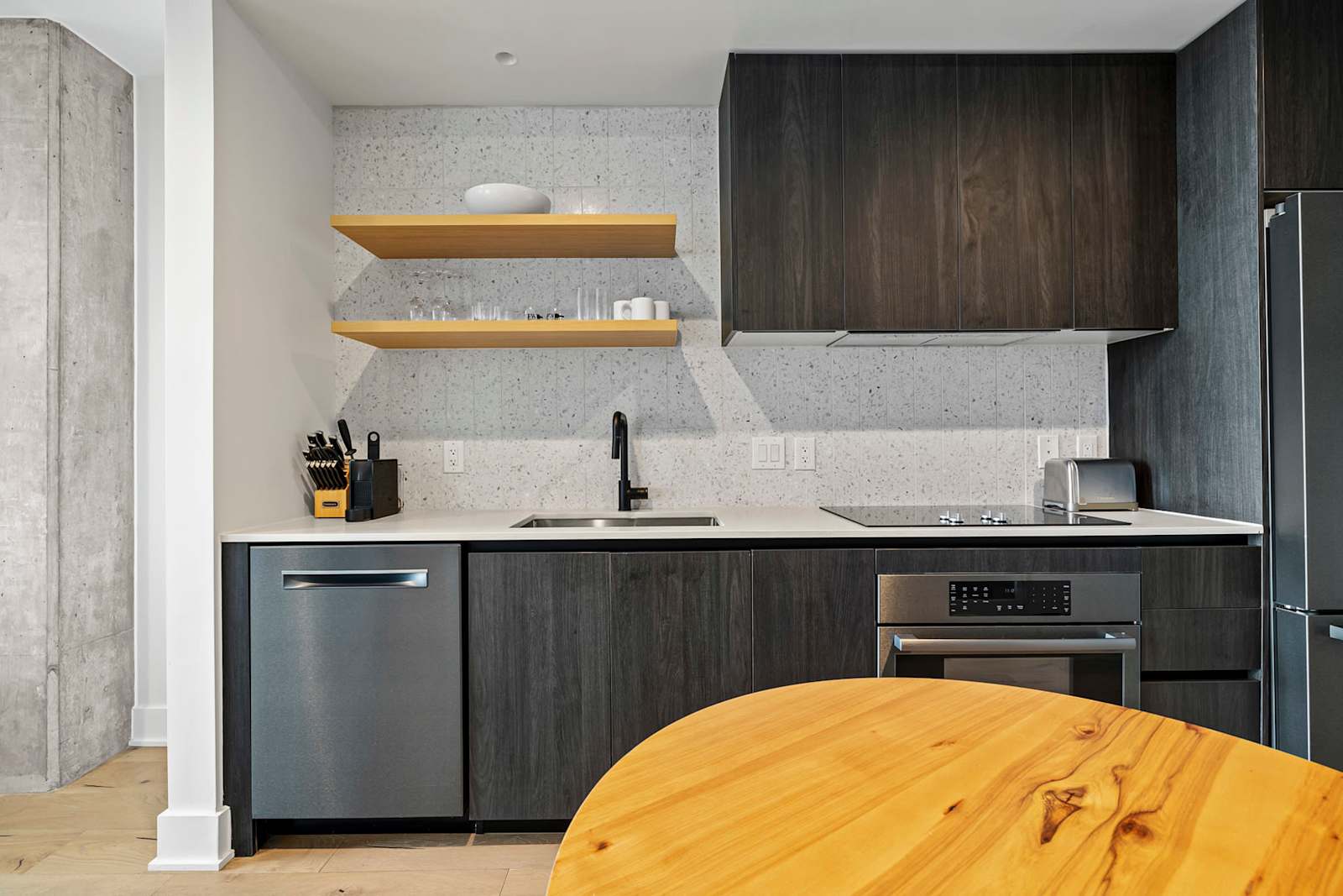 Kitchen detail in unit 1204 showing the dishwasher, induction cooktop, open shelving and oak dining table
