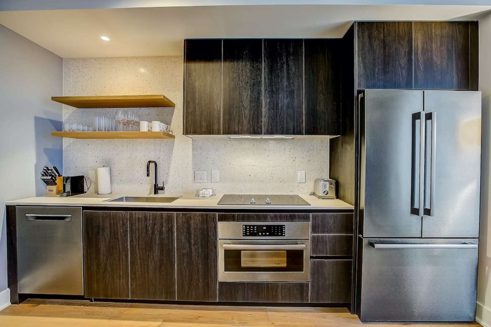 Kitchen in unit 1406 with dark cabinetry, induction cooktop, wall oven and full-height refrigerator