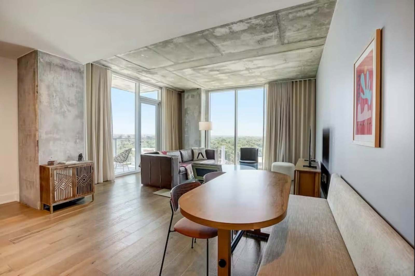 Dining table and living area of unit 1504 with exposed concrete ceiling and windows on two sides