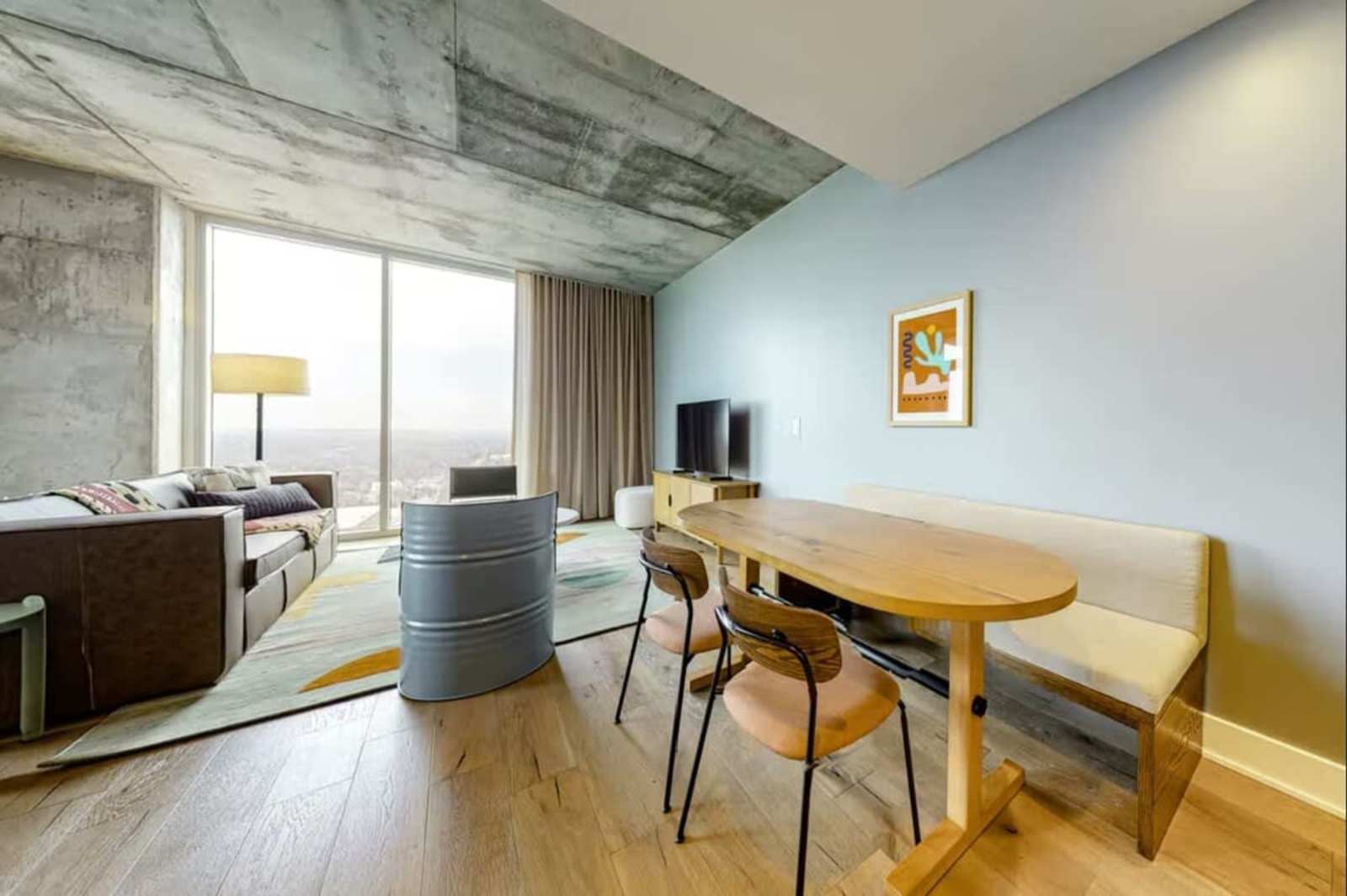 Living and dining area of unit 1205 with an oak table, dining chairs and exposed concrete ceiling
