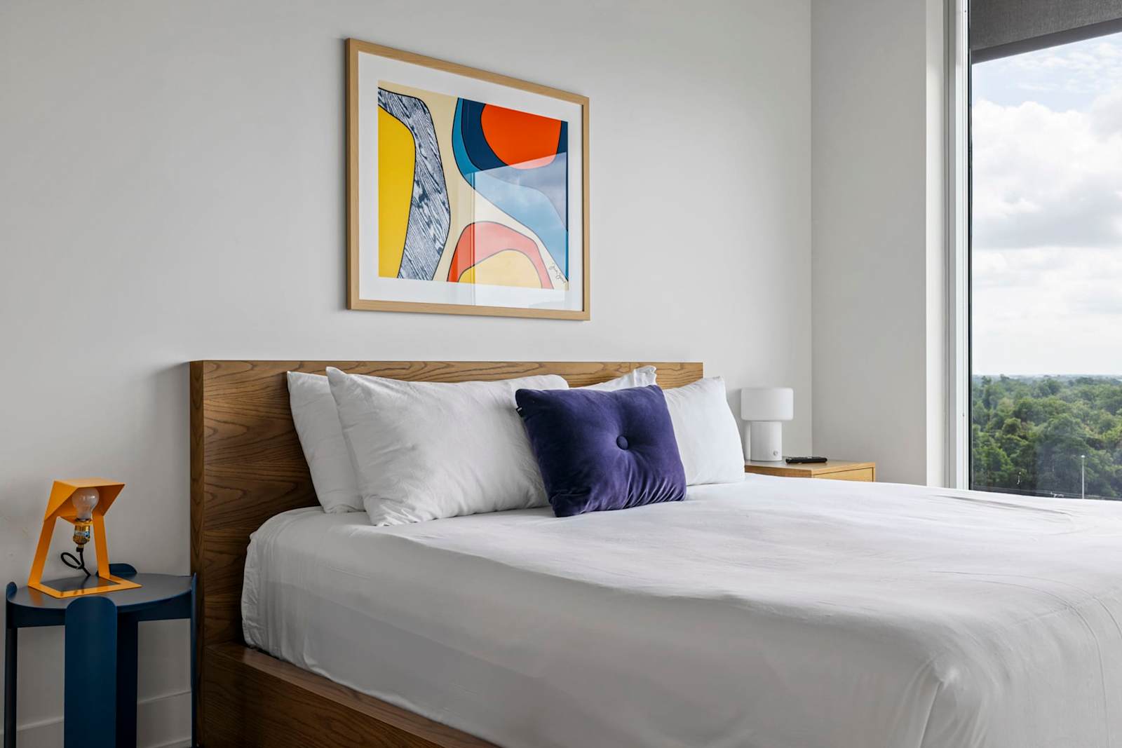 Queen bed in unit 1204 with white linens, framed artwork and daylight from the corner window