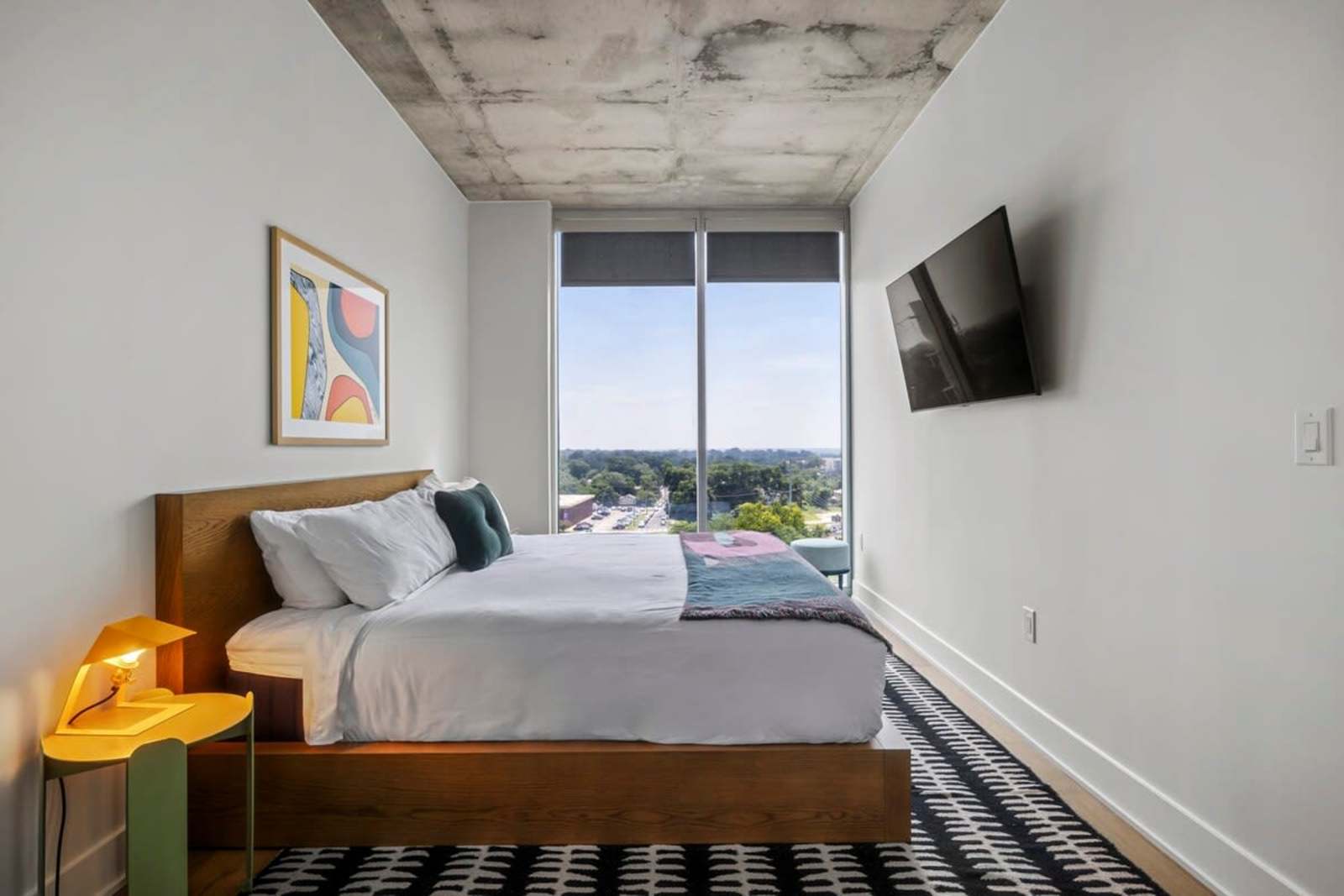 Bedroom in unit 1105 with a wall-mounted TV, upholstered headboard and a window looking over the tree line