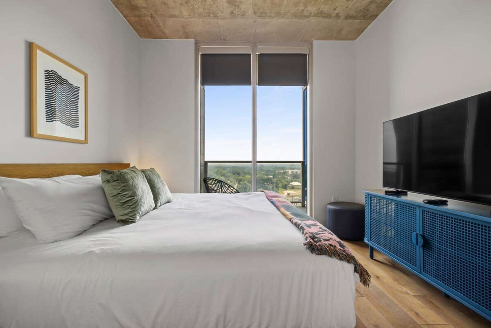 Bedroom in unit 1409 with a large wall-mounted TV, blue console and a shaded window