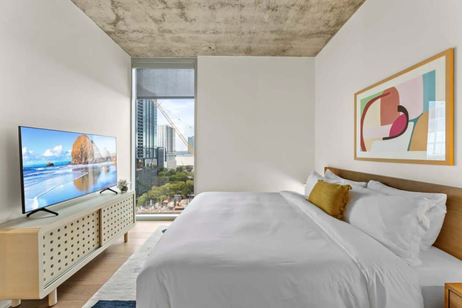 Bedroom in unit 1804 with a large wall-mounted TV opposite the bed and downtown visible through the window