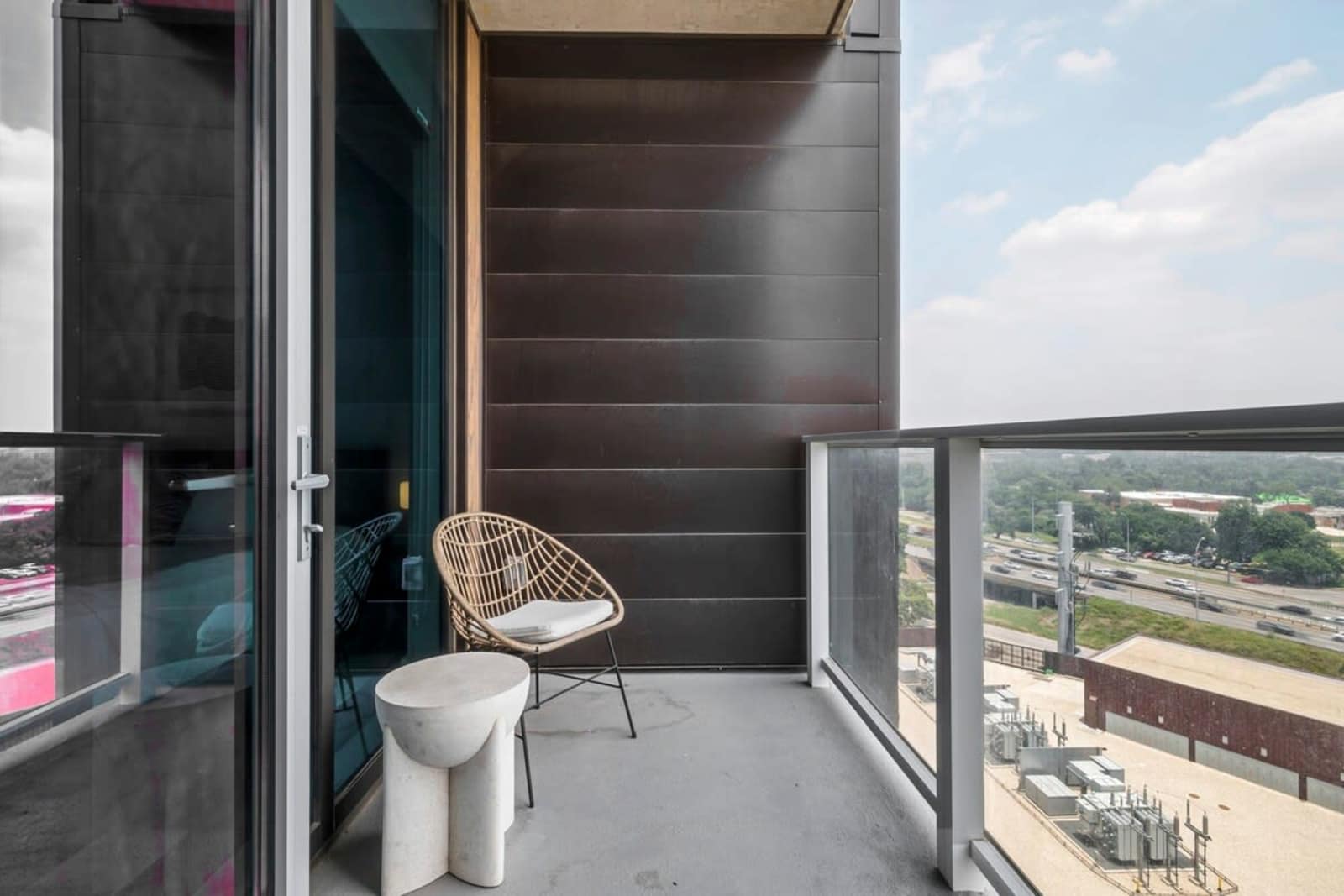 Private balcony of unit 1409 with a woven chair and side table, looking down over the city