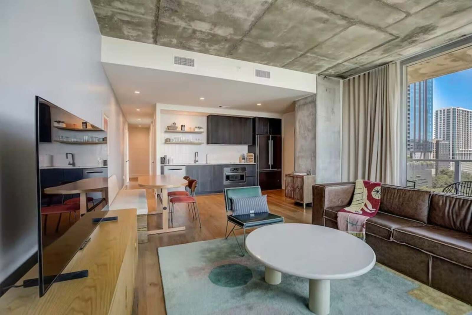 Living room of unit 1504 looking toward the kitchen, with a media wall and pale rug