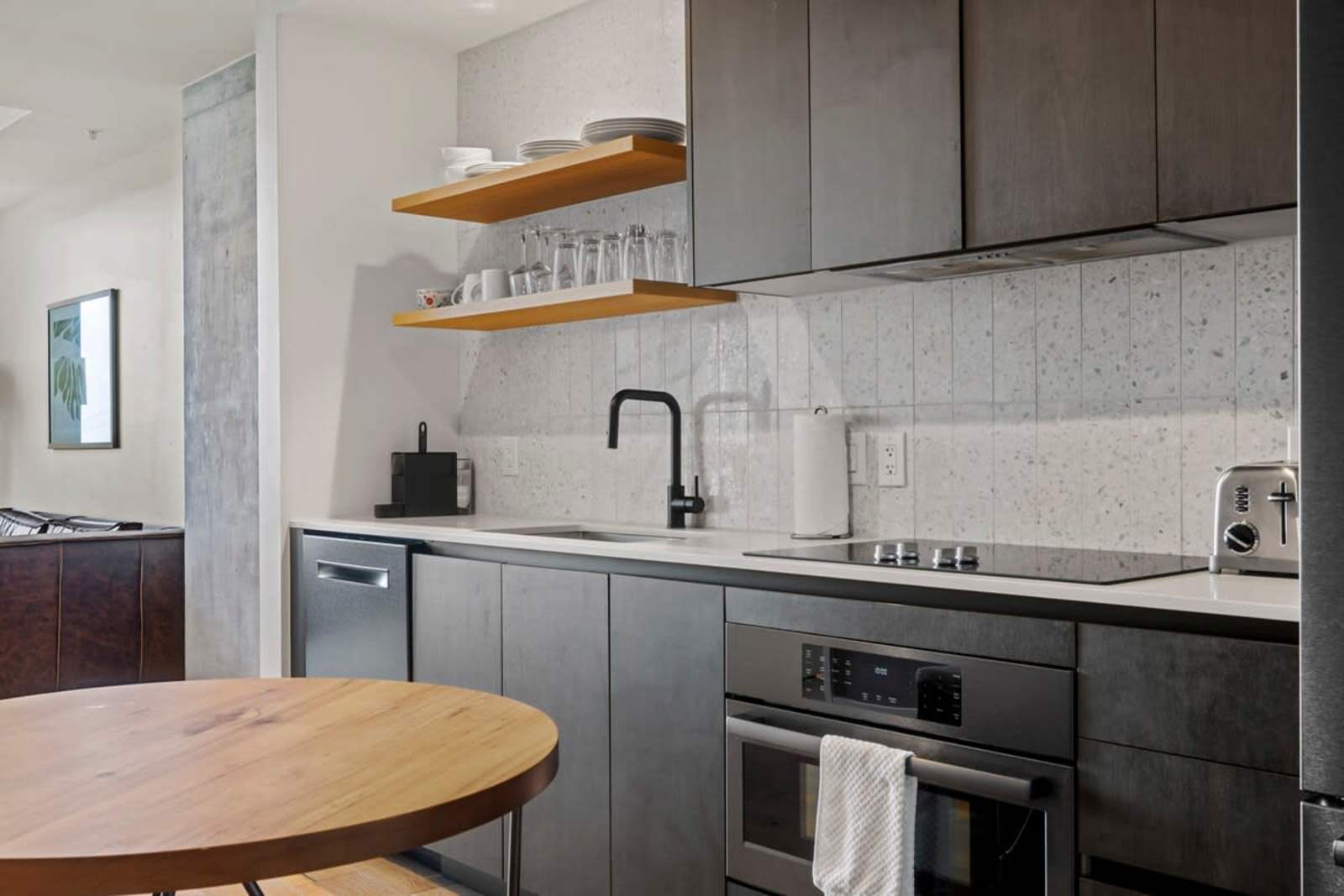 Kitchen counter in unit 1105 with induction cooktop, wall oven, open shelving and dining table