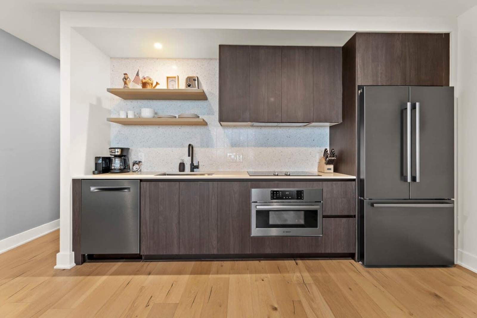 Kitchen in unit 1804 with dark cabinetry, wall oven, induction cooktop and full-height refrigerator