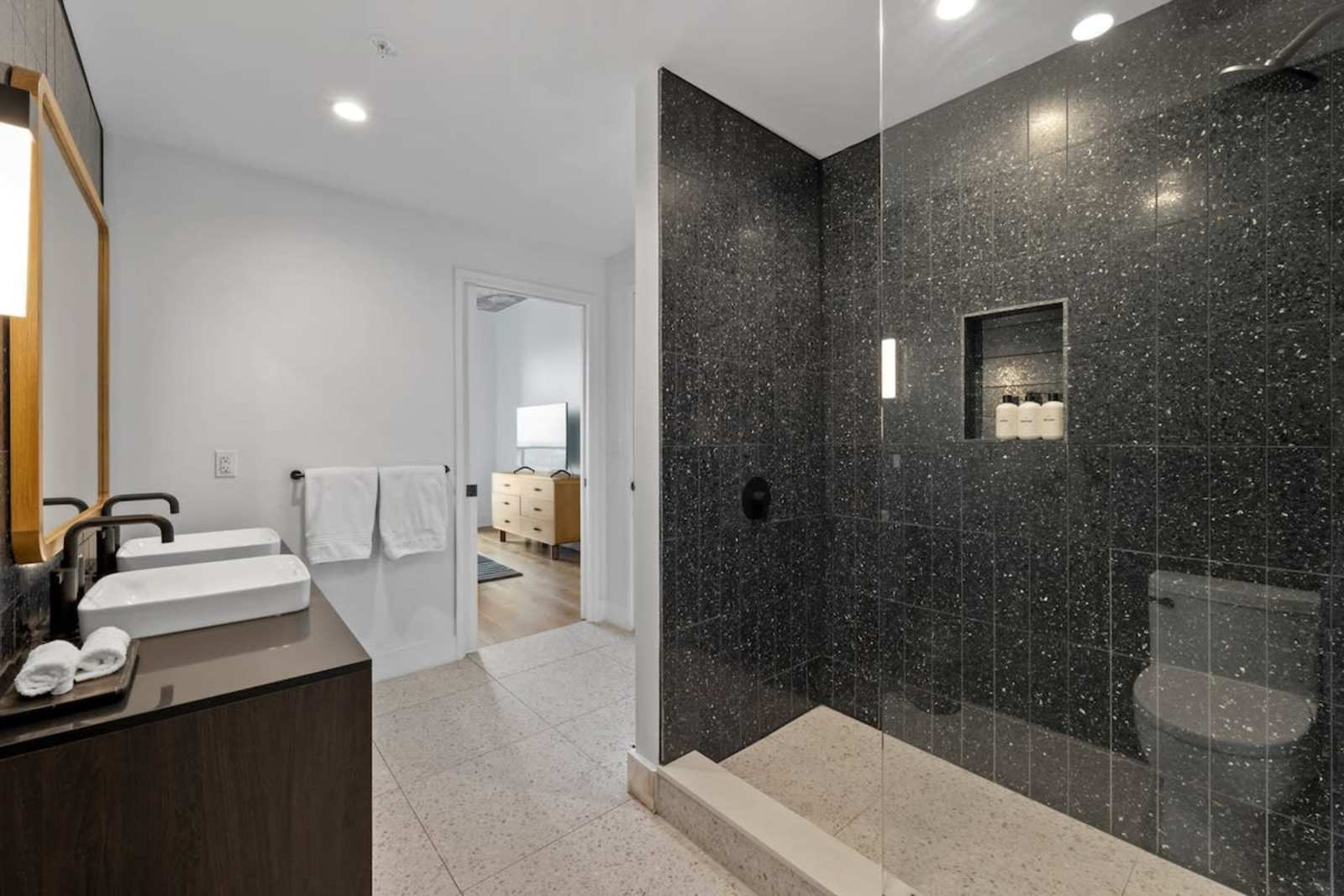 Walk-in shower in unit 2006 finished in dark speckled stone, beside the vanity