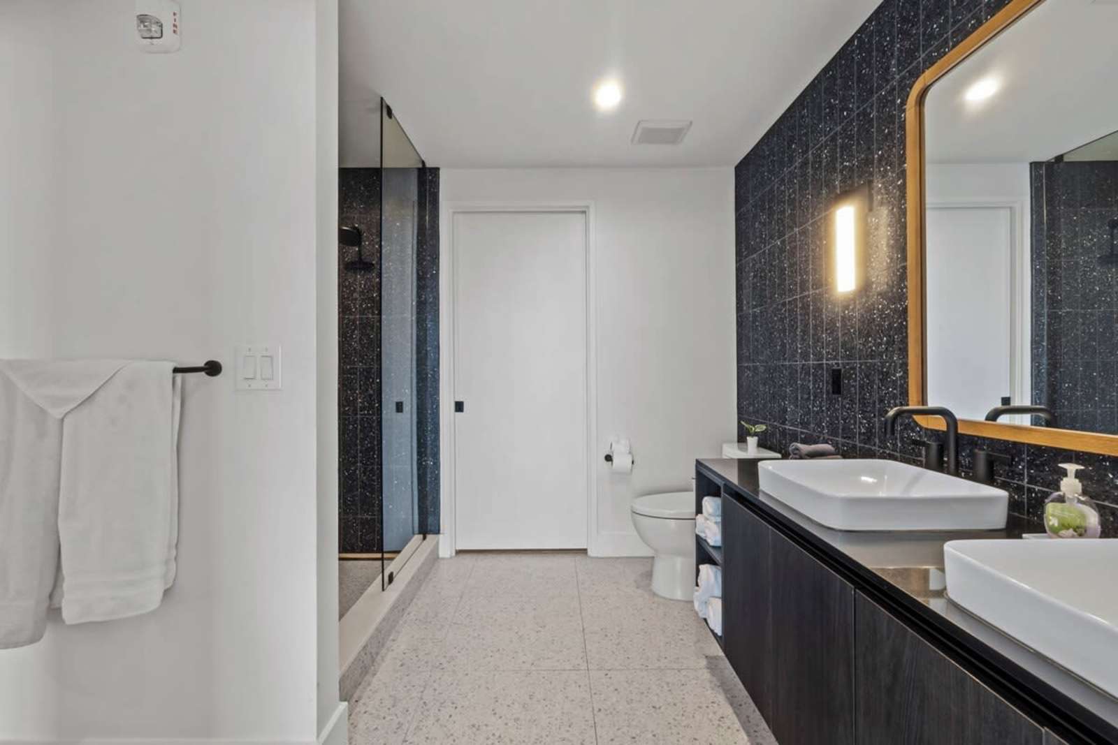 Walk-in shower and bathroom entry in unit 1105 with folded towels and terrazzo flooring
