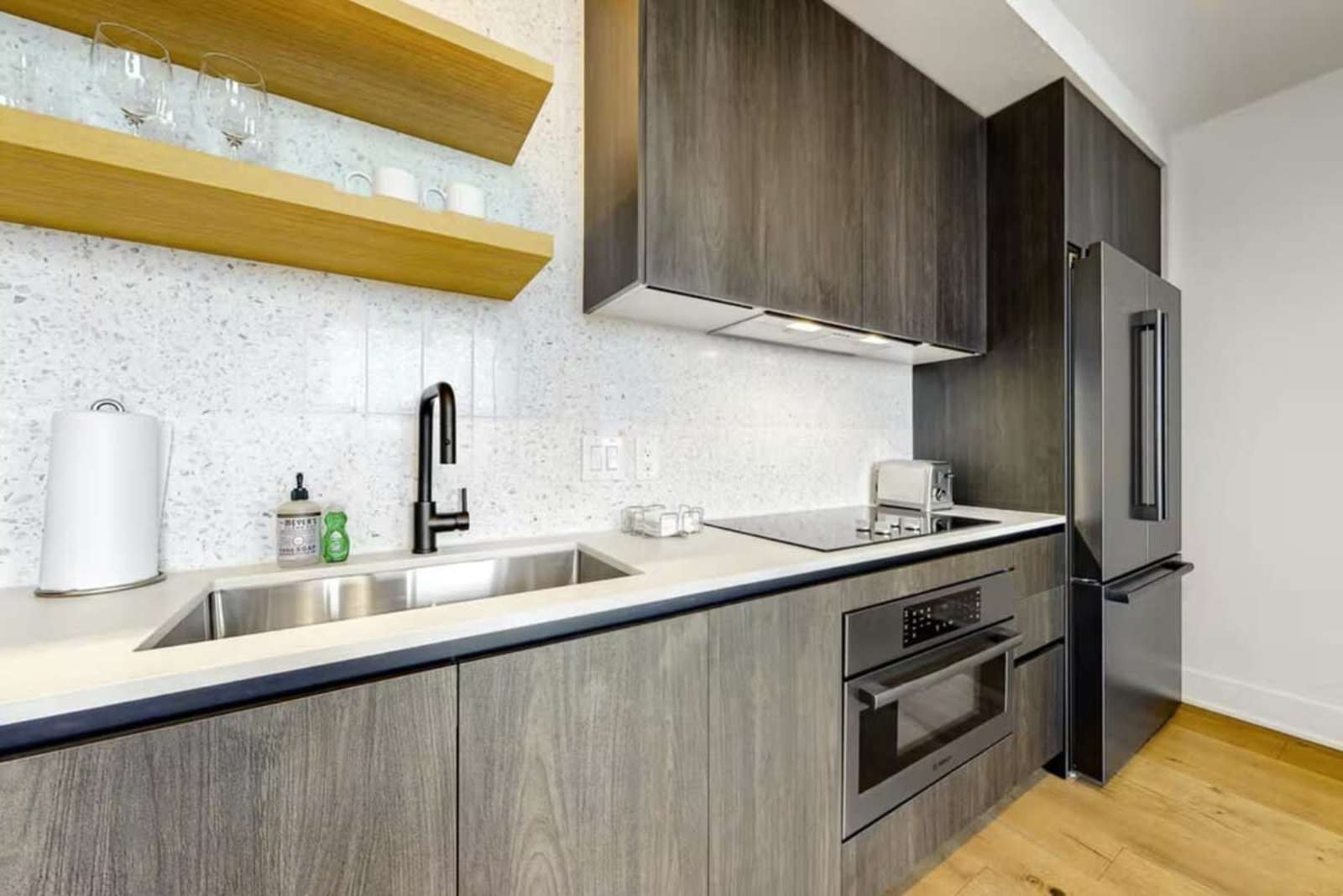 Kitchen counter detail in unit 1205 with sink, induction cooktop, tiled backsplash and open shelving